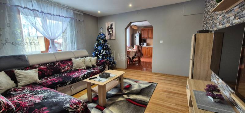 A családi ház nappalijában van egy kanapé, egy karácsonyfa és egy fa dekorációjú padló.