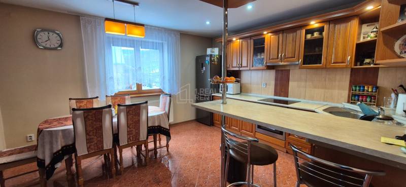 Konyha étkezőasztallal családi házban, fa szekrények és csempézett padló.