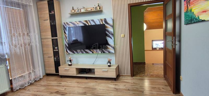 Nappali egy családi házban fa dekor padlóval és nagy televízióval a falon.