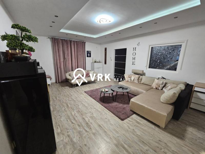 Nappali egy családi házban, fa dekorációjú padlóval és nagy kanapéval.