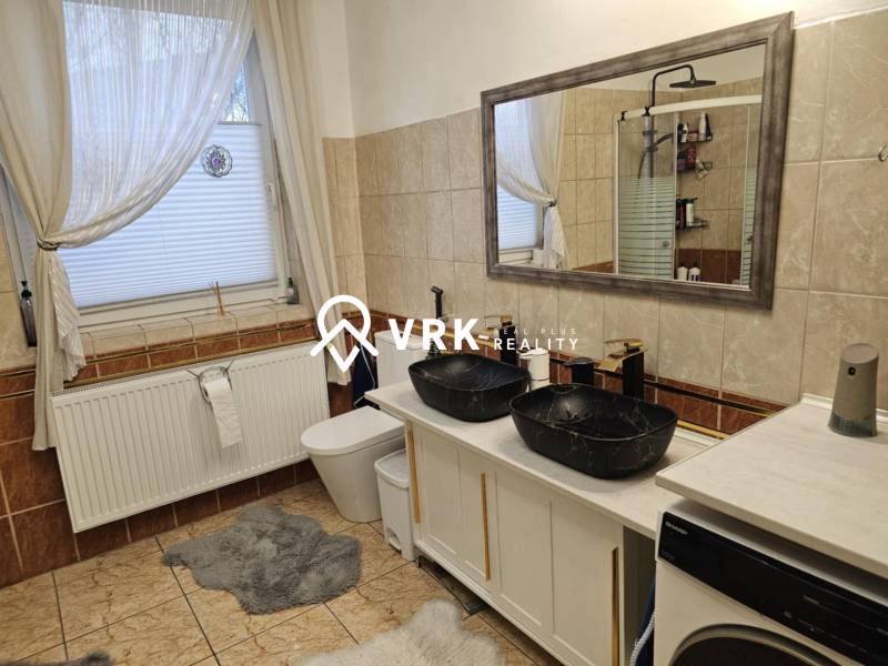 Fürdőszoba családi házban dupla mosdóval, káddal és mosógéppel a csempén.