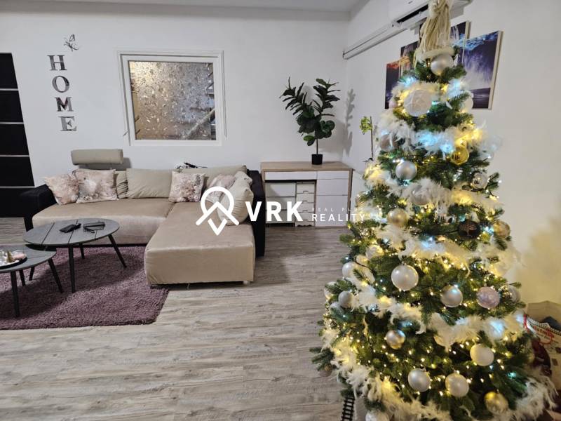 Egy családi házban, amelynek padlója fa dekorációval van ellátva, egy feldíszített karácsonyfa és egy kanapé található.