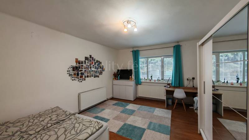 Egy szoba családi házban íróasztallal, ággyal, falon lévő fényképekkel és fa dekoros padlóval.