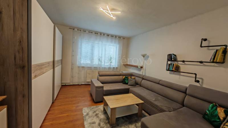 Nappali egy családi házban kanapéval, könyvespolccal és fa dekorációjú padlóval.