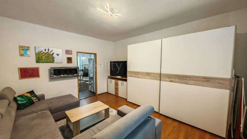 Nappali egy családi házban, fa mintázatú padlóval, kanapéval és képekkel a falon.