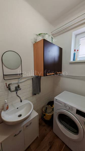 Fürdőszobai helyiség mosdóval, mosógéppel és szekrénnyel, fa dekoros padlóval.