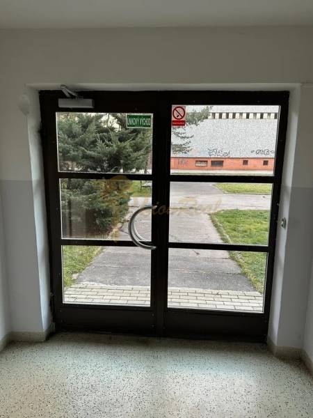 Üveg bejárati ajtó belülről, a kijárat egy gondozott gyephez és járdához vezet.