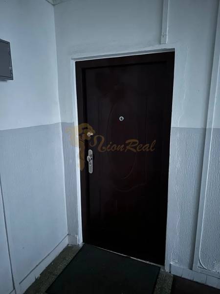 Bejárati ajtó egy kétszobás lakásban fehér falakkal és barna szőnyeggel.