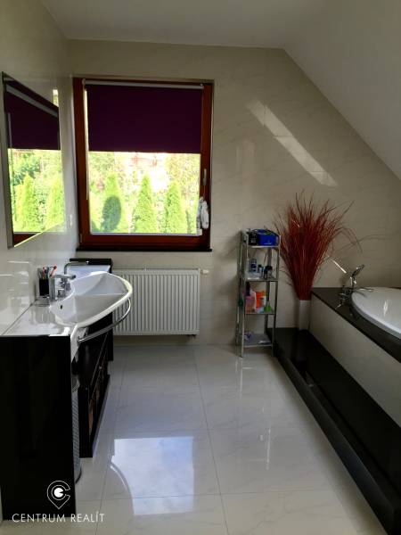 Fürdőszoba családi házban káddal, mosdóval, polccal és ablakkal, lila rolóval.