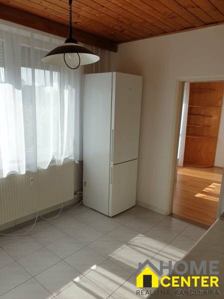 Konyha függönnyel és hűtőszekrénnyel egy egyszobás lakásban, fa mintázatú padlóval.