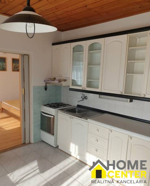 Konyha egy egyszobás lakásban fehér szekrényekkel, tűzhellyel és fa dekoros padlóval.