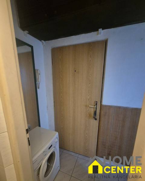 Előszoba egy egyszobás lakásban mosógéppel, ajtókkal és csempézett padlóval.