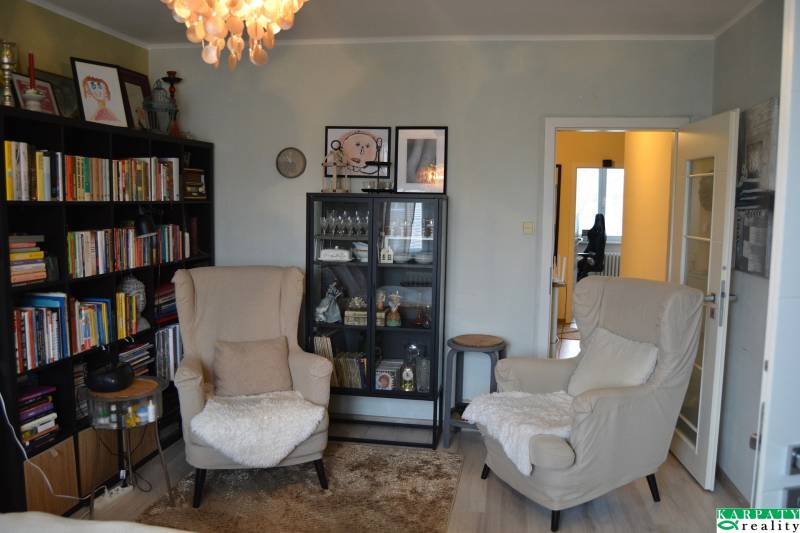 Nappali egy háromszobás lakásban könyvespolcokkal és fa mintázatú padlóval.