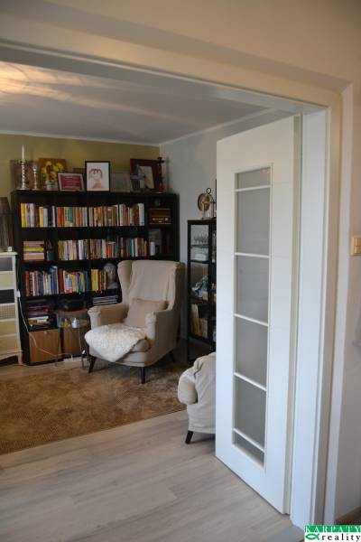 Olvasósarok kényelmes fotellel és könyvekkel egy háromszobás lakásban, fa mintázatú padlóval.