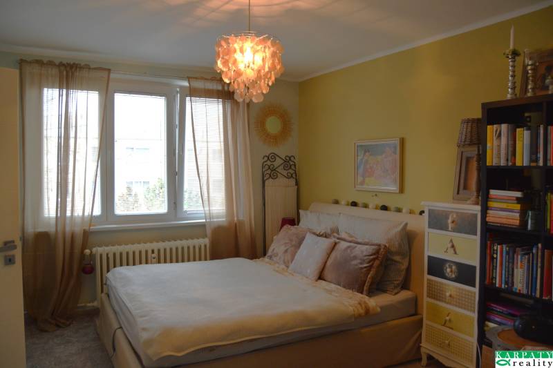 Hangulatos hálószoba függönyökkel és könyvespolccal egy háromszobás lakásban, a hangulatot egy érdekes csillár teszi teljessé.