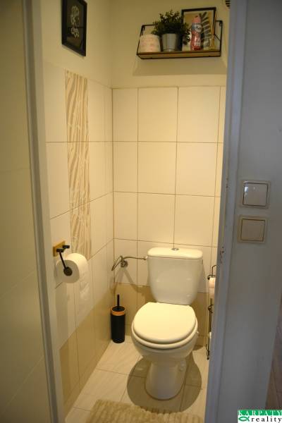 Fürdőszoba WC-vel egy háromszobás lakásban, világos csempék, polcok, dekoratív elemek.