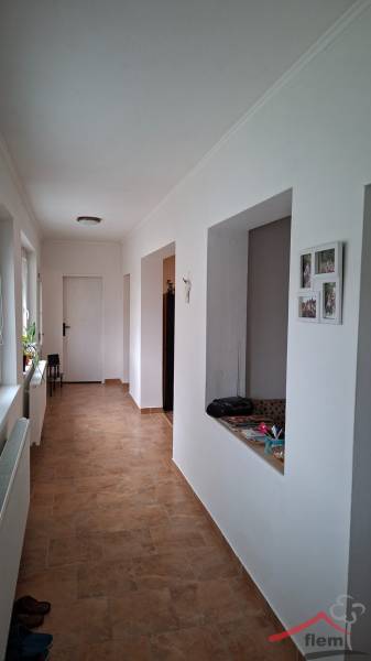 Családi ház folyosója csempével és fehér falakkal, a jobb oldalon nyitott ajtókkal.