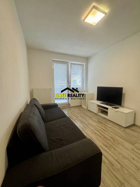 Nappali egy kétszobás lakásban kanapéval, televízióval és fa mintázatú padlóval.