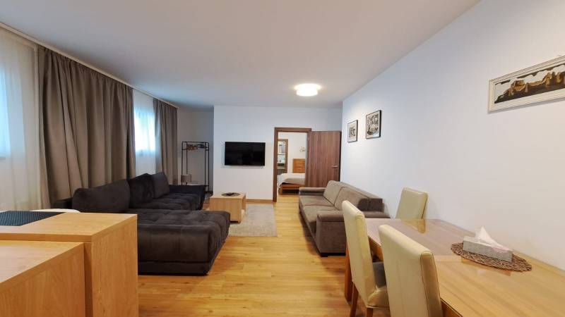 Nappali kanapéval és TV-vel, étkezőasztal mellett, fa dekorációjú padlóval.