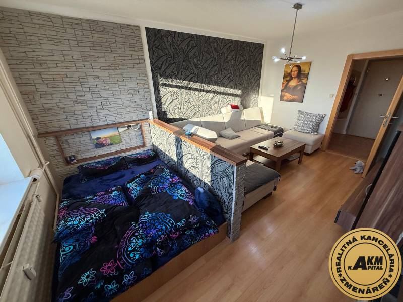 Nappali kanapéval, ággyal és fa dekorációjú padlóval egy háromszobás lakásban.