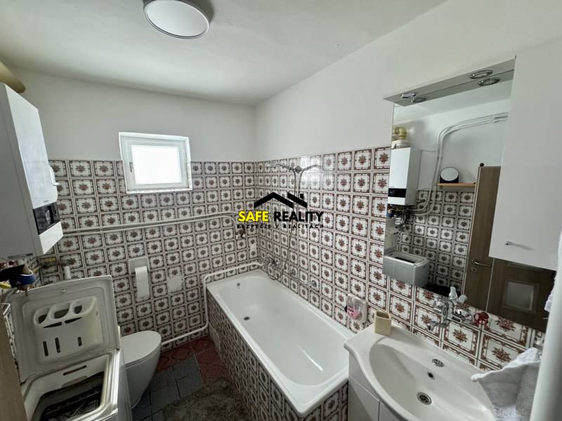 Fürdőszoba családi házban csempézett falakkal, káddal és mosógéppel.