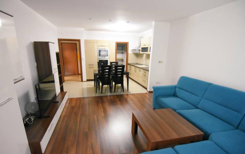 Nappali egy kétszobás lakásban, fa mintázatú padlóval és kék kanapéval.