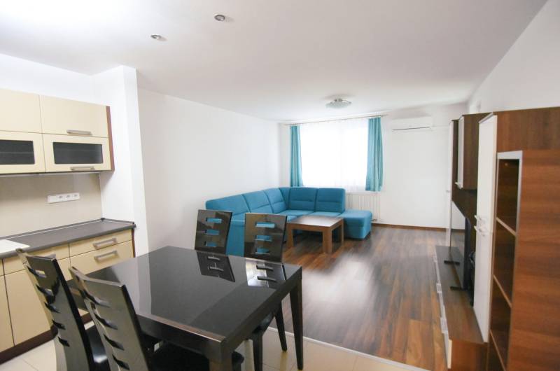 Nappali kék kanapéval, konyhával és fa dekoros padlóval egy kétszobás lakásban.