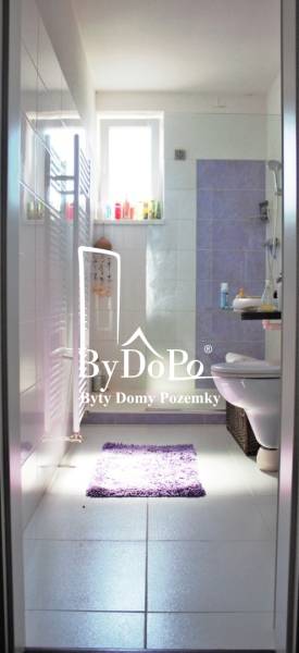 Fürdőszoba egy egyszobás lakásban WC-vel, mosdóval és ablakkal. A világos csempék dominálnak.