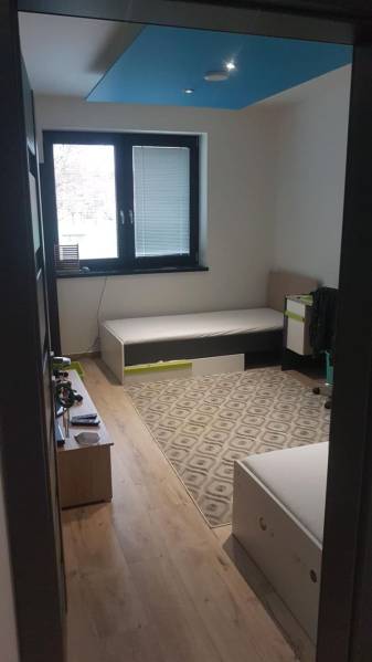 Szoba egy családi házban fa dekoros padlóval, ágyakkal, szőnyeggel és ablakkal.