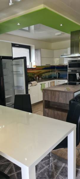 Családi ház konyhája nyitott hűtőszekrénnyel, zöld mennyezettel és étkezőasztallal.