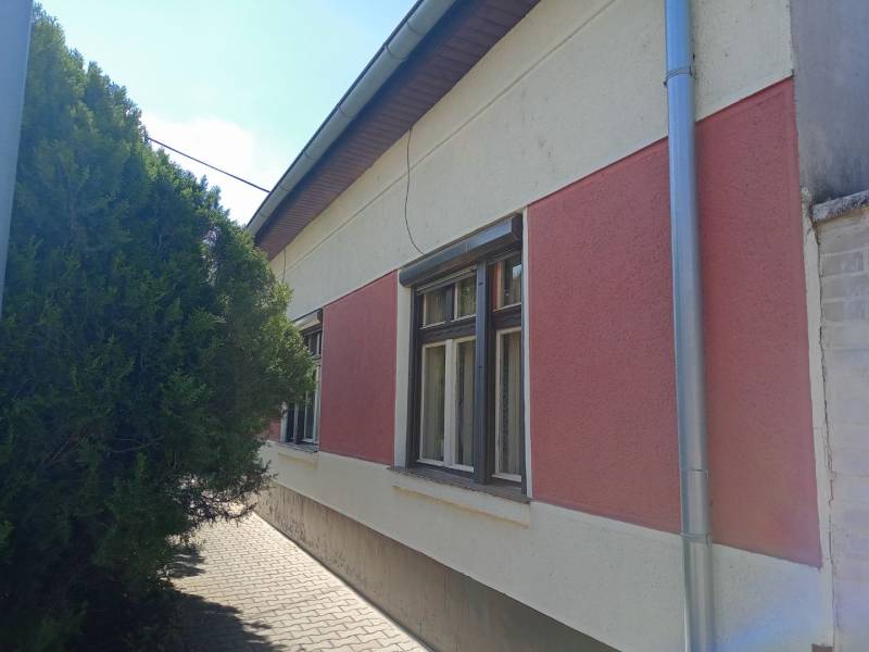 Családi ház Érsekújváron szigetelt homlokzattal és hálókkal, valamint fával a járda mellett.