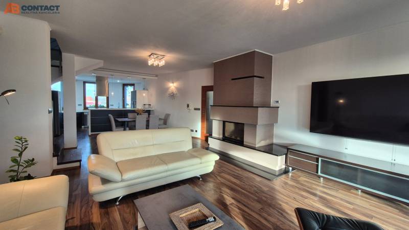 Tágas nappali kandallóval egy családi házban, világos bútorokkal, fa mintázatú padlóval.