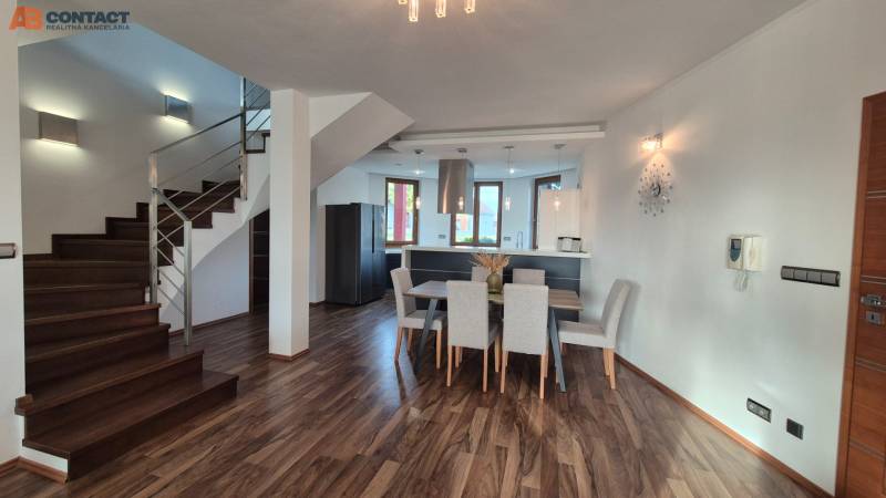 Családi ház belső tere konyhával, étkezővel és lépcsővel, fa dekorral a padlón.