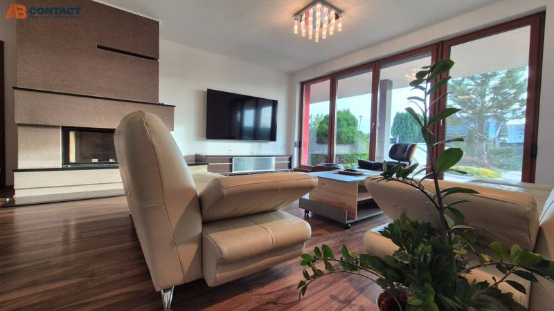 Nappali családi házban bőrkanapéval, kandallóval, televízióval és fa dekorációjú padlóval.