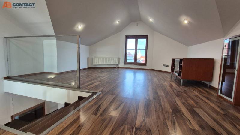 Tetőtéri szoba fa dekorációjú padlóval, lépcsővel és nagy ablakkal.