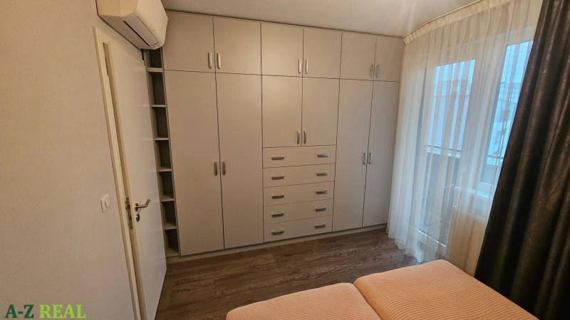 Hálószoba fehér beépített szekrénnyel és ággyal egy háromszobás lakásban, fa dekoros padlóval.