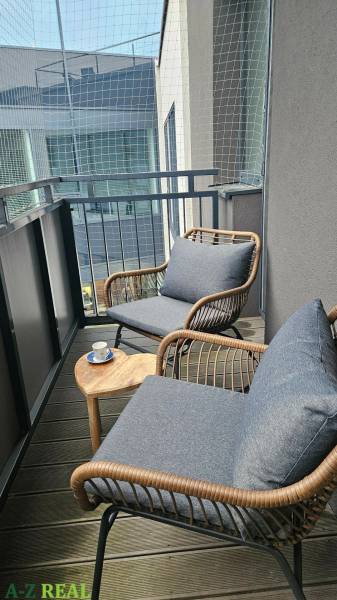 Erkély kényelmes székekkel és asztallal egy háromszobás lakásban, fa dekoros padlóval.