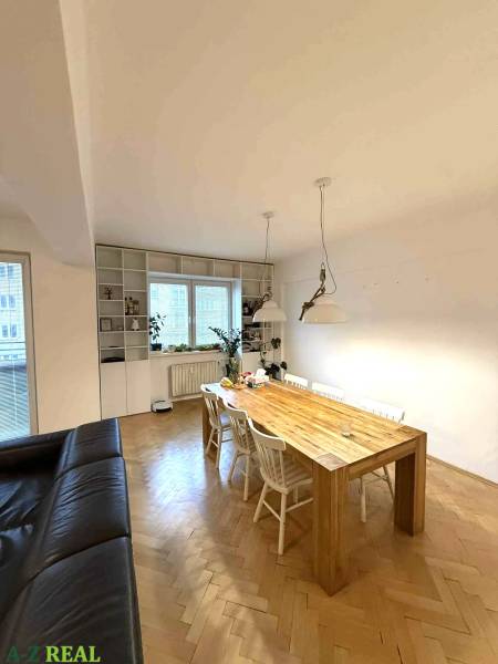 Étkezőasztal egy négy szobás lakásban, fa dekorral ellátott padlóval és fehér székekkel.