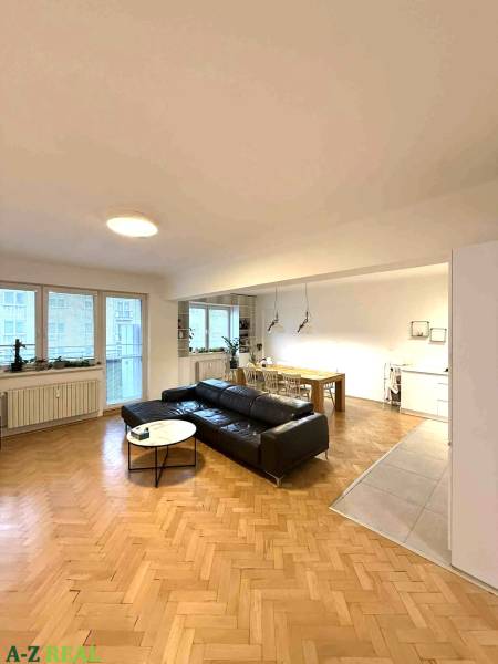 Nappali egy 4 szobás lakásban, fa dekoros padlóval és fekete kanapéval.