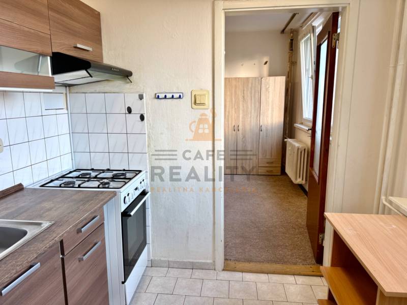 Konyha fehér csempékkel, tűzhellyel, szekrényekkel és kilátással az előszobára egy egyszobás lakásban.