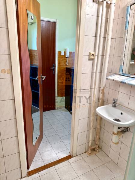 Fürdőszoba egy egyszobás lakásban tükörrel, mosdóval és fehér csempékkel.