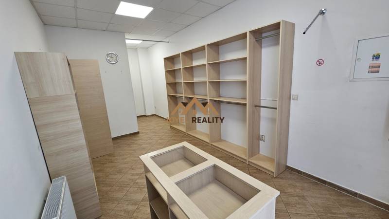 Kereskedelmi helyiség polcokkal és fa dekorációjú padlóval, fehér fal, mennyezeti világítás.