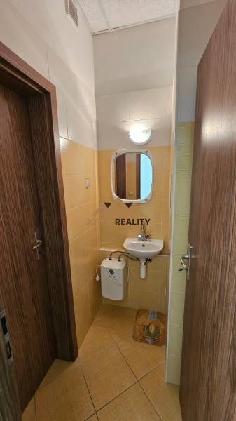 Egy kereskedelmi helyiségben található fürdőszoba mosdóval és tükörrel, világos csempékkel burkolva.