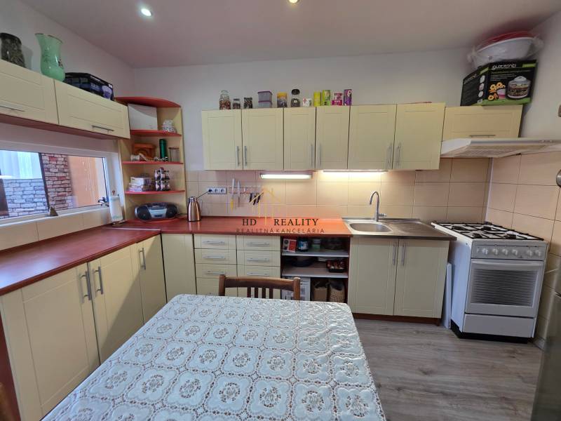 Konyha egy háromszobás lakásban krémszínű konyhabútorral és fa mintázatú padlóval.