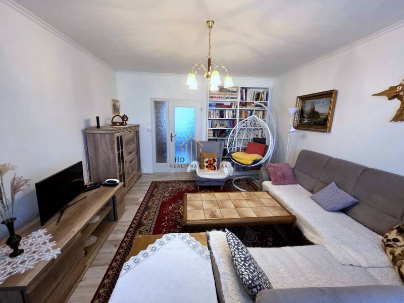 Nappali egy háromszobás lakásban fa mintázatú padlóval és könyvespolcokkal.