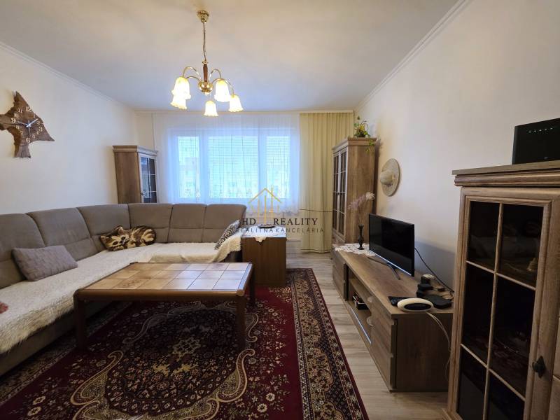 Nappali egy háromszobás lakásban sarokkanapéval és fa mintázatú padlóval.