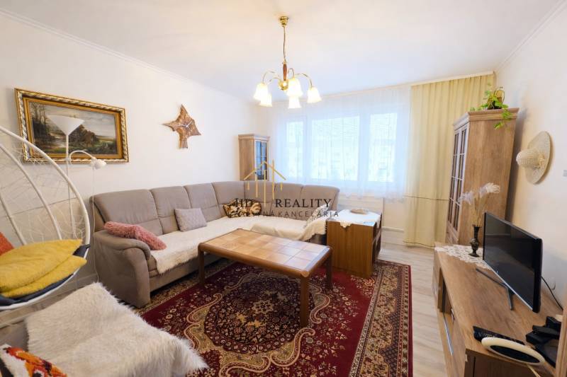 Nappali egy háromszobás lakásban kanapéval, piros szőnyeggel és mennyezeti lámpával.