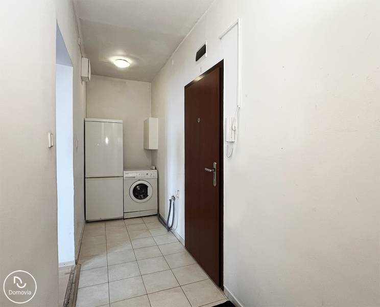 Az egyszobás lakás előszobája mosógéppel és hűtőszekrénnyel. Fehér falak, kerámia padló.