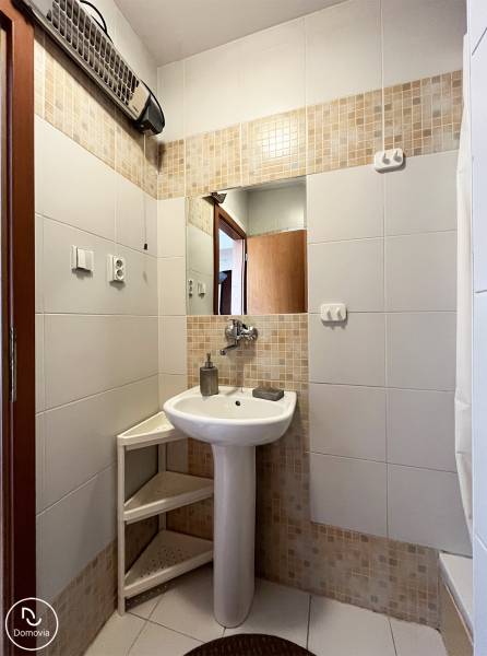 Fürdőszoba egy egyszobás lakásban mosdóval, tükörrel és fehér csempékkel.