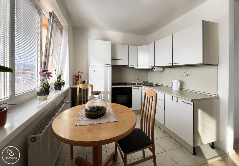 Konyha egy egyszobás lakásban ablakokkal, asztallal és növényekkel a párkányon.